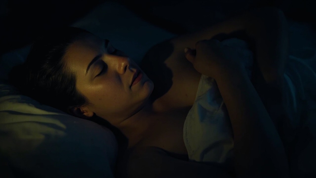 Person lying in bed at night with eyes closed, hand resting on the belly, breathing slowly in low warm light