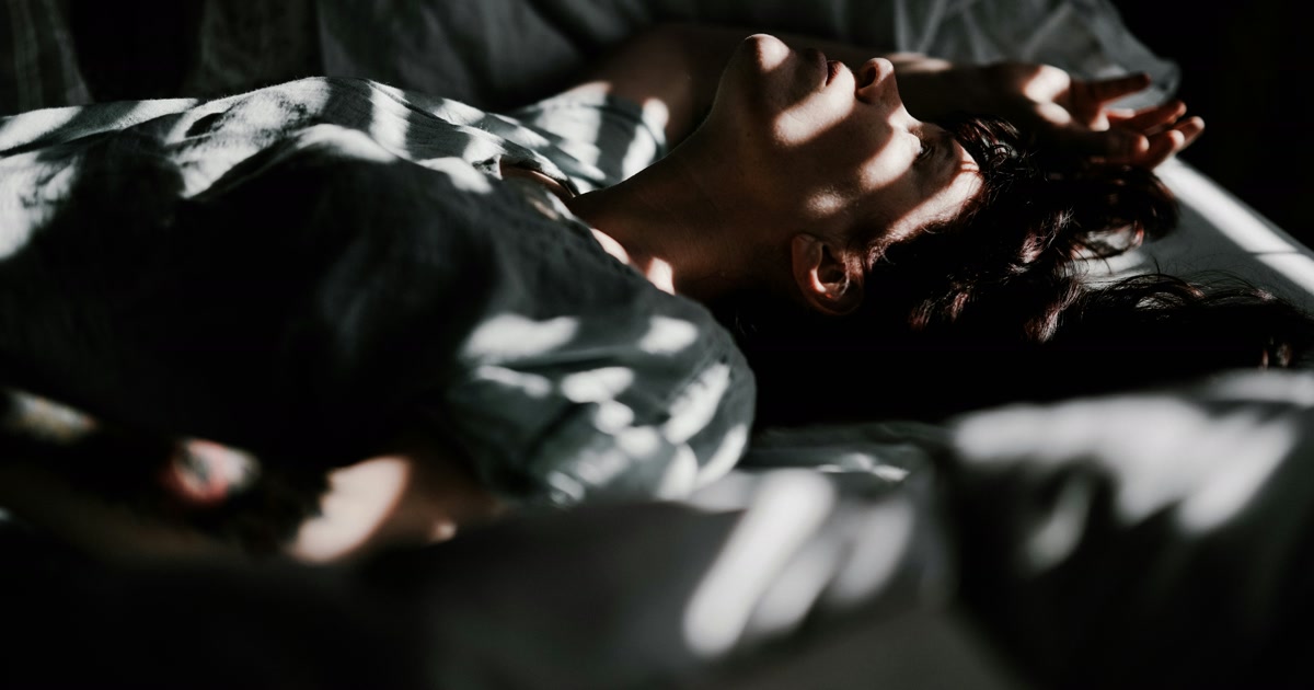 Person lying awake in bed exhausted but alert soft moonlight